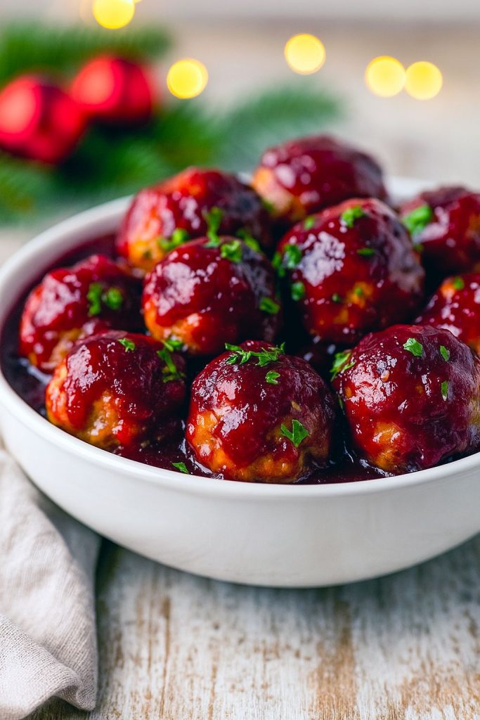 Glossy cranberry-glazed meatballs piled on a festive platter, garnished with chopped parsley and ready for serving.
