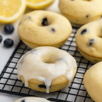 Close-up of a glazed lemon blueberry doughnut with visible berries and a shiny lemon glaze on a wooden board.