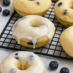 Close-up of a glazed lemon blueberry doughnut with visible berries and a shiny lemon glaze on a wooden board.