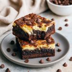 Close-up of fudgy chocolate brownie squares topped with a marbled cream-cheese layer, arranged on parchment and ready to serve.