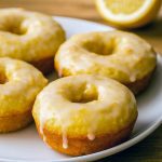 Glazed baked lemon donuts and mini donut holes on a cooling rack with lemon zest and shiny glaze.