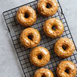 Maple-glazed baked pumpkin donut with glossy glaze, sitting on a wooden board and sprinkled with chopped pecans.